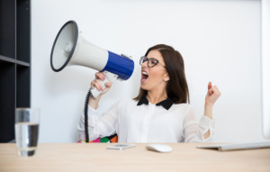 Businesswoman sitting at the table and speaking through megaphone